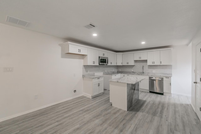 kitchen with appliances with stainless steel finishes, white cabinets, a kitchen island, sink, and light stone counters