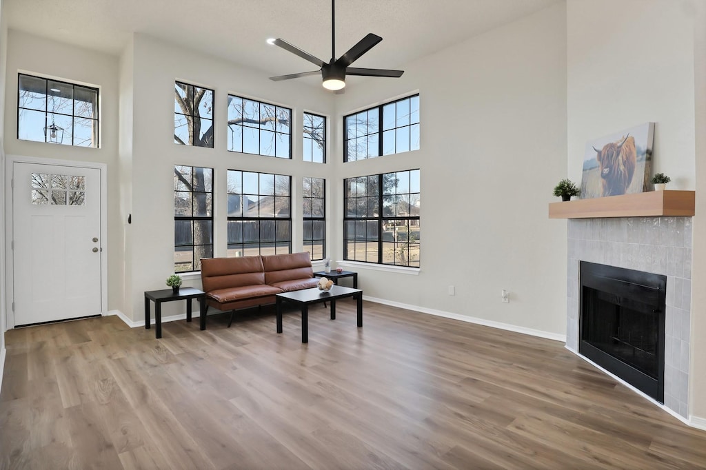 living room with wood-type flooring, a tiled fireplace, a towering ceiling, and ceiling fan