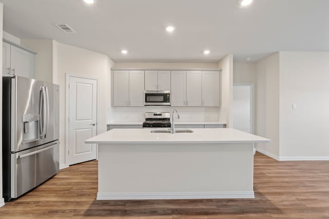 kitchen featuring sink, appliances with stainless steel finishes, light wood-type flooring, and an island with sink