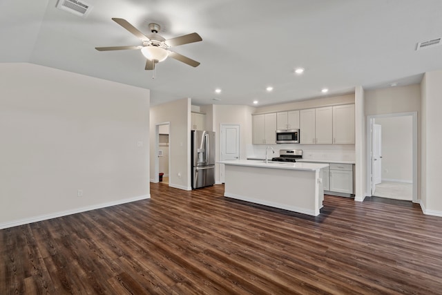 kitchen featuring ceiling fan, appliances with stainless steel finishes, white cabinets, dark wood-type flooring, and an island with sink