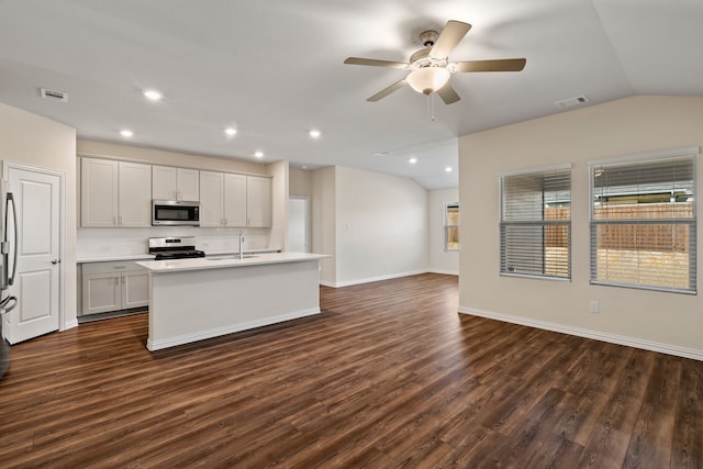 kitchen featuring ceiling fan, vaulted ceiling, appliances with stainless steel finishes, an island with sink, and dark hardwood / wood-style floors