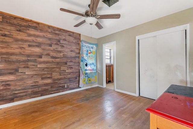 interior space with wood-type flooring, wood walls, and ceiling fan