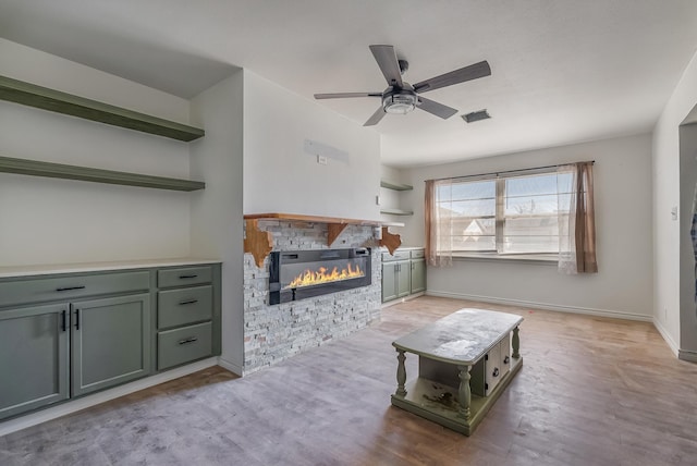 living room with ceiling fan, a stone fireplace, and light wood-type flooring