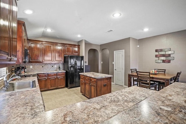 kitchen featuring vaulted ceiling, sink, tasteful backsplash, a kitchen island, and black fridge