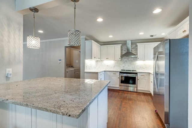 kitchen with appliances with stainless steel finishes, white cabinets, decorative light fixtures, washer and dryer, and wall chimney exhaust hood