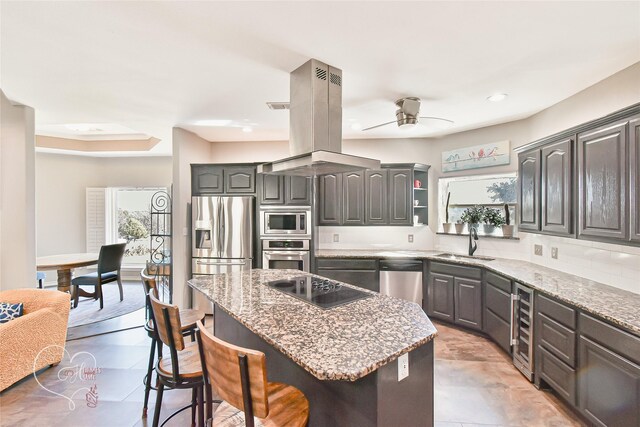 kitchen with appliances with stainless steel finishes, sink, island exhaust hood, a kitchen island, and a breakfast bar area