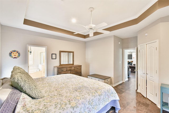 bedroom with a closet, ceiling fan, ensuite bathroom, a tray ceiling, and ornamental molding