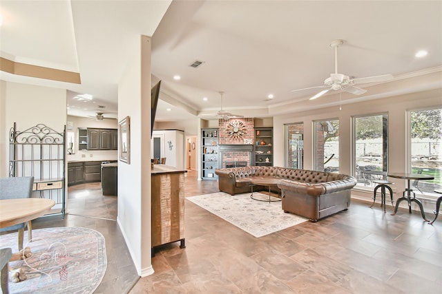 living room featuring ceiling fan, a fireplace, a raised ceiling, built in features, and ornamental molding