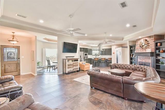 living room featuring ornamental molding, a brick fireplace, ceiling fan, and a raised ceiling