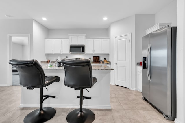 kitchen with light stone counters, stainless steel appliances, an island with sink, and white cabinets