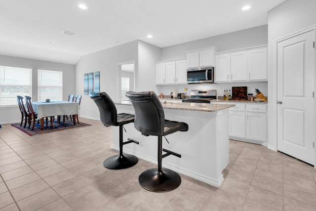 kitchen with a breakfast bar area, appliances with stainless steel finishes, white cabinetry, light stone counters, and a kitchen island