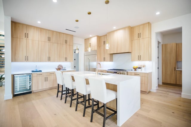 kitchen featuring light brown cabinets, light wood-type flooring, a center island with sink, and beverage cooler