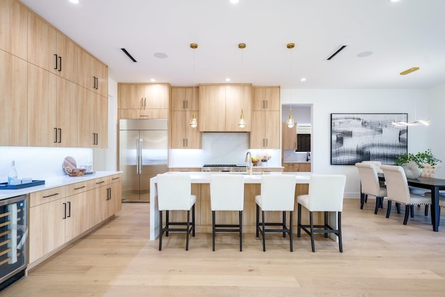 kitchen featuring decorative light fixtures, stainless steel built in fridge, light brown cabinetry, and beverage cooler