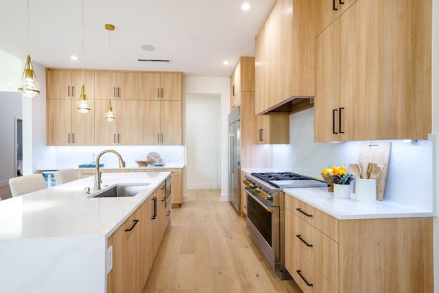 kitchen featuring light brown cabinets, hanging light fixtures, high quality appliances, sink, and light wood-type flooring