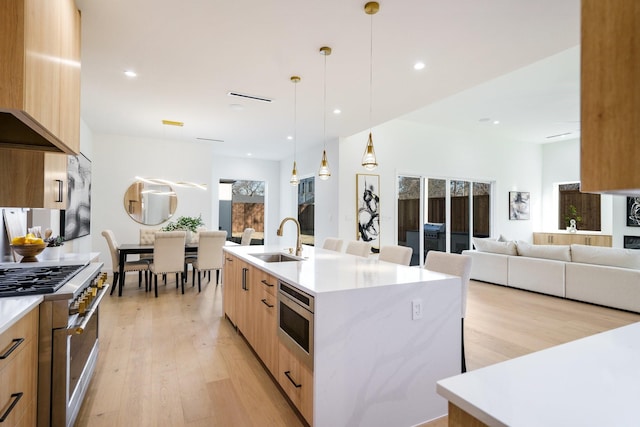 kitchen featuring a kitchen island with sink, sink, decorative light fixtures, stainless steel appliances, and a breakfast bar area