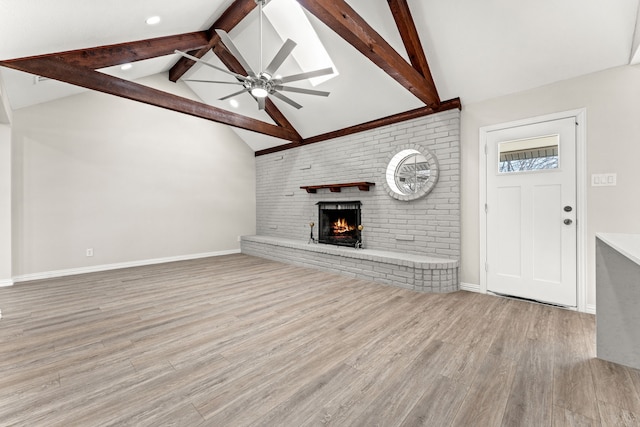 unfurnished living room featuring a brick fireplace, light hardwood / wood-style floors, lofted ceiling with beams, and ceiling fan