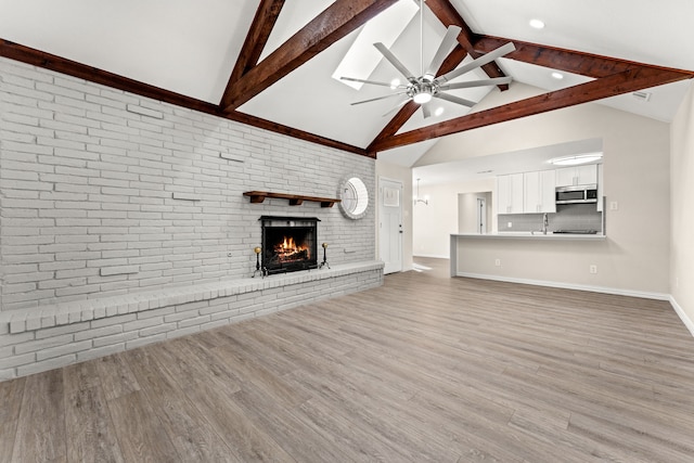 unfurnished living room with hardwood / wood-style floors, a fireplace, sink, ceiling fan, and beam ceiling