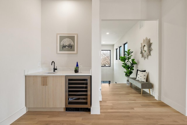 bar with light brown cabinetry, sink, light hardwood / wood-style floors, and beverage cooler