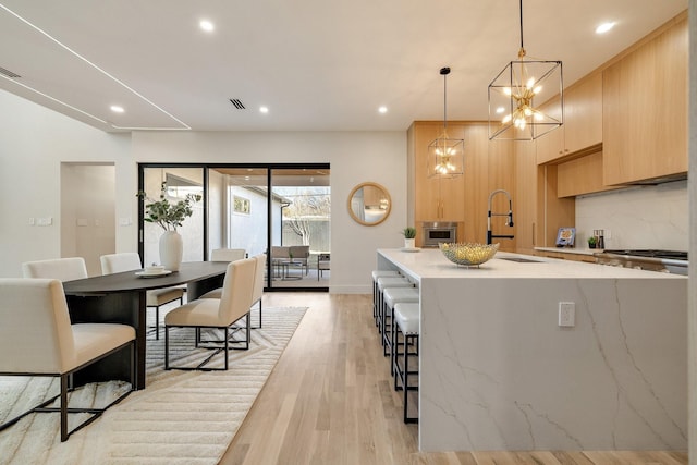 kitchen featuring a kitchen bar, light hardwood / wood-style flooring, light brown cabinets, an island with sink, and pendant lighting