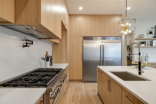 kitchen with stainless steel appliances, light stone countertops, sink, and decorative light fixtures