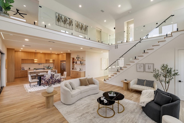 living room with a towering ceiling, light hardwood / wood-style floors, and ceiling fan