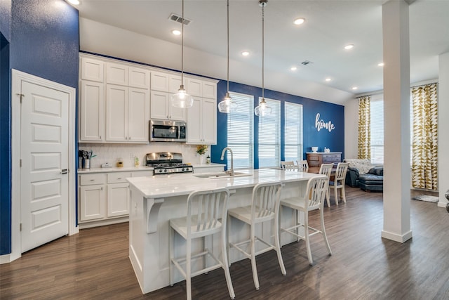 kitchen with pendant lighting, sink, white cabinetry, stainless steel appliances, and a center island with sink