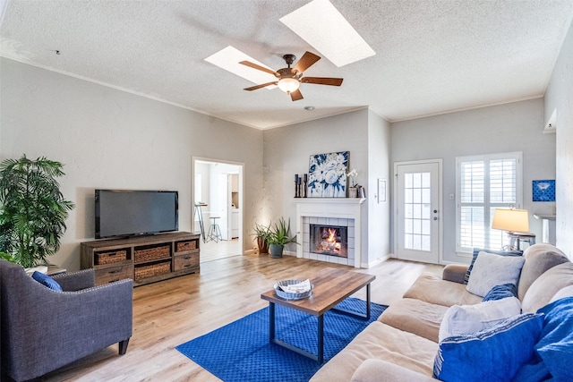 living room featuring a fireplace, light hardwood / wood-style floors, a textured ceiling, and a skylight