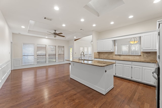 kitchen featuring dark stone countertops, white cabinetry, a center island with sink, and a tray ceiling