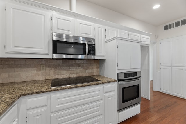 kitchen with white cabinets, dark wood-type flooring, stainless steel appliances, dark stone countertops, and decorative backsplash