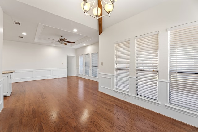 unfurnished living room with ceiling fan with notable chandelier, dark wood-type flooring, and a tray ceiling