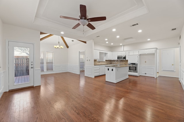 kitchen featuring a kitchen island with sink, decorative backsplash, white cabinets, stainless steel appliances, and a tray ceiling