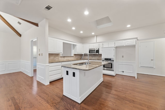 kitchen with stone countertops, appliances with stainless steel finishes, sink, white cabinetry, and a kitchen island with sink