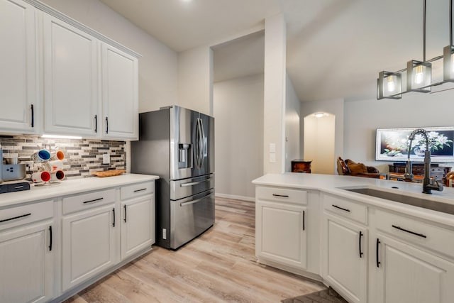 kitchen with hanging light fixtures, sink, white cabinets, light wood-type flooring, and stainless steel fridge with ice dispenser