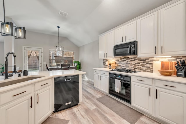 kitchen with decorative light fixtures, sink, black appliances, and vaulted ceiling