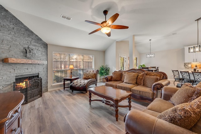 living room featuring light wood-type flooring, ceiling fan with notable chandelier, vaulted ceiling, and a stone fireplace