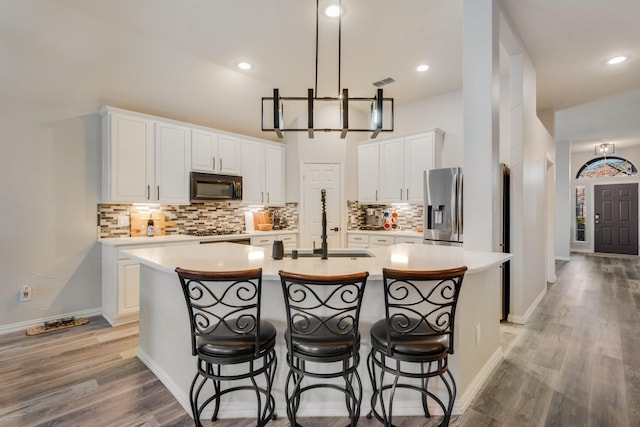 kitchen featuring white cabinets, an island with sink, and stainless steel fridge