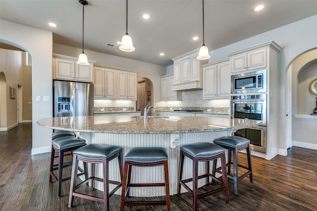 kitchen featuring stainless steel appliances, hanging light fixtures, light stone countertops, and a large island with sink