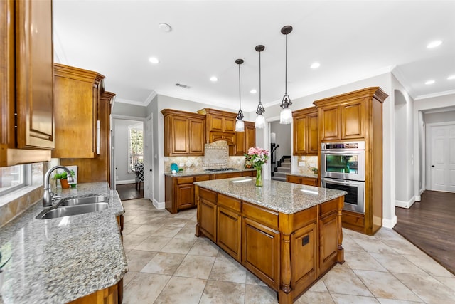 kitchen featuring a kitchen island, brown cabinets, decorative light fixtures, stainless steel appliances, and a sink