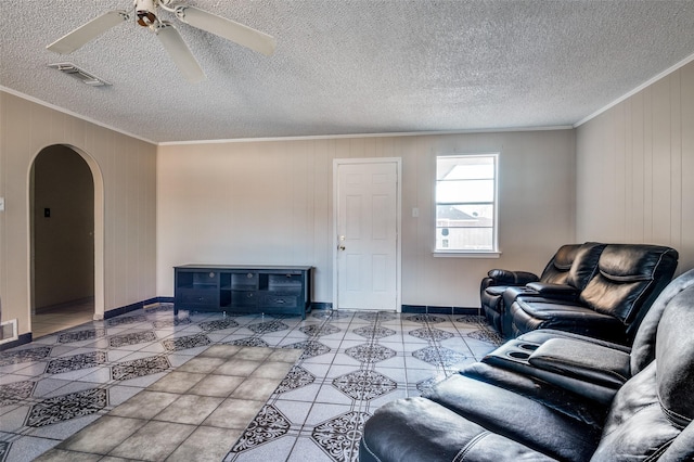 living room featuring ceiling fan, crown molding, wooden walls, and a textured ceiling