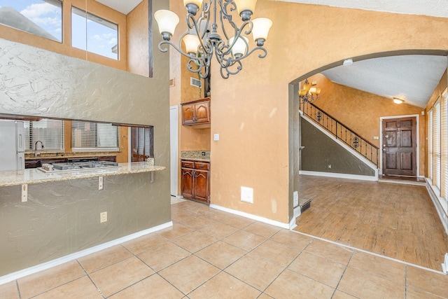 interior space with light tile patterned floors, light stone counters, decorative light fixtures, vaulted ceiling, and white fridge