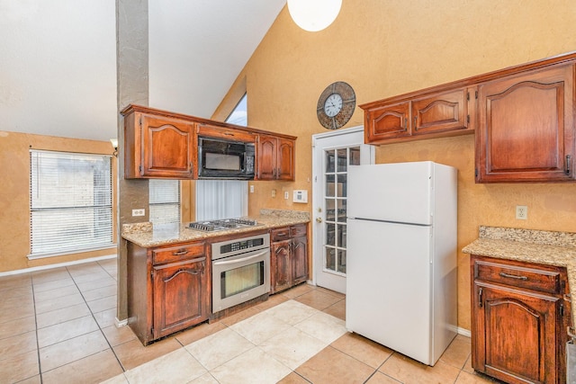 kitchen featuring light tile patterned flooring, lofted ceiling, appliances with stainless steel finishes, and light stone countertops