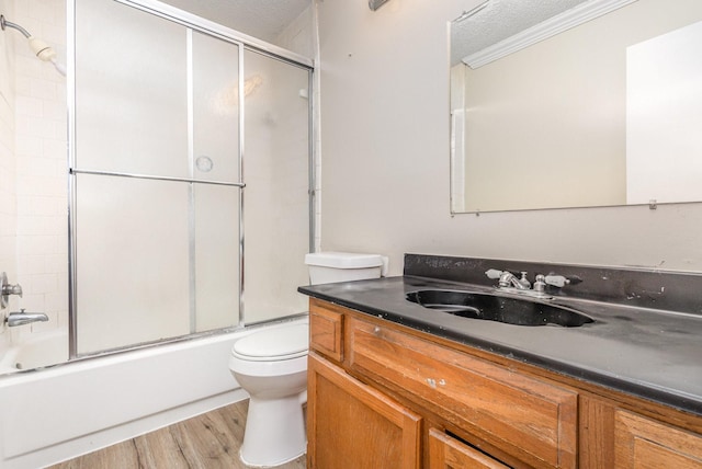 full bathroom featuring toilet, combined bath / shower with glass door, a textured ceiling, ornamental molding, and vanity