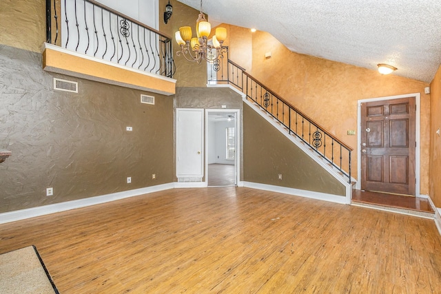 unfurnished living room with hardwood / wood-style flooring, high vaulted ceiling, an inviting chandelier, and a textured ceiling