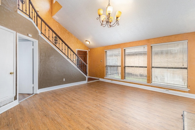 unfurnished living room with wood-type flooring, a textured ceiling, vaulted ceiling, and a chandelier