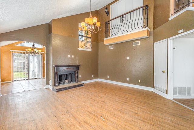 unfurnished living room featuring high vaulted ceiling, hardwood / wood-style flooring, a textured ceiling, and a chandelier