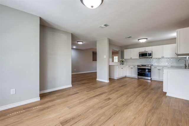 kitchen with tasteful backsplash, white cabinets, sink, light hardwood / wood-style flooring, and stainless steel appliances