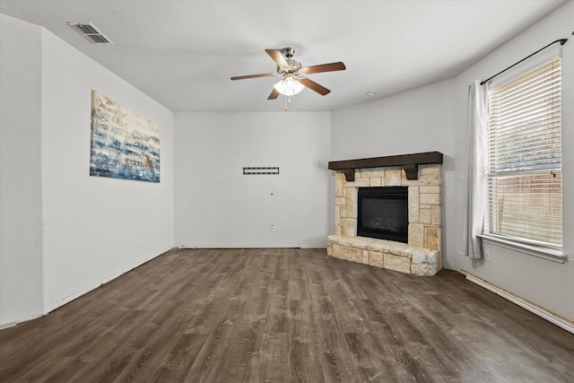 unfurnished living room with ceiling fan, a healthy amount of sunlight, a stone fireplace, and dark hardwood / wood-style flooring