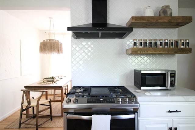 kitchen with tasteful backsplash, white cabinetry, wall chimney range hood, and appliances with stainless steel finishes