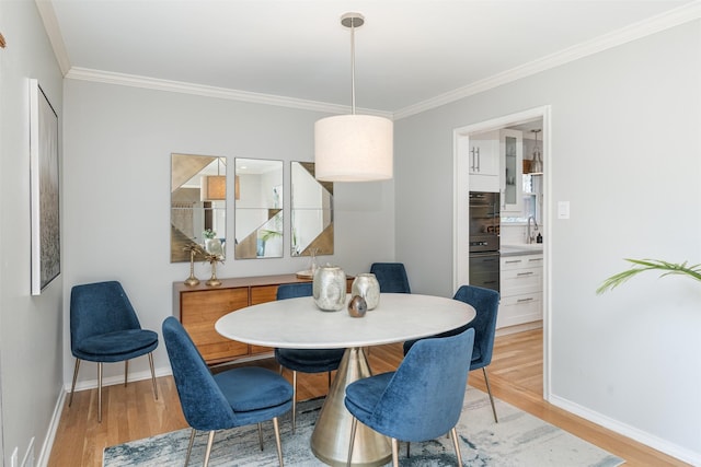 dining space with ornamental molding, light hardwood / wood-style flooring, and sink