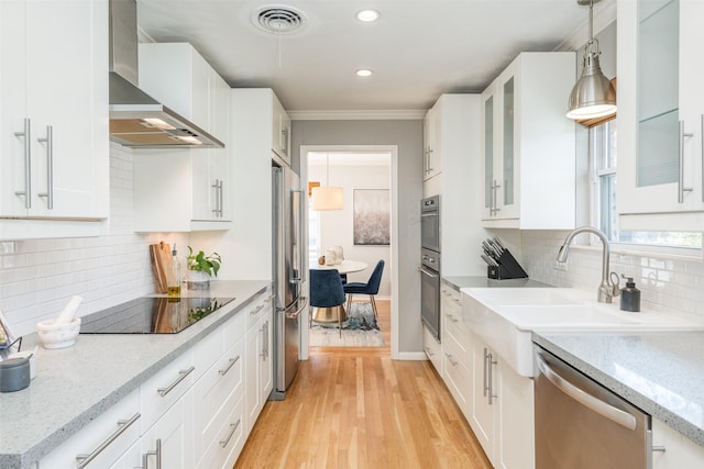 kitchen with light stone countertops, white cabinets, appliances with stainless steel finishes, wall chimney range hood, and hanging light fixtures